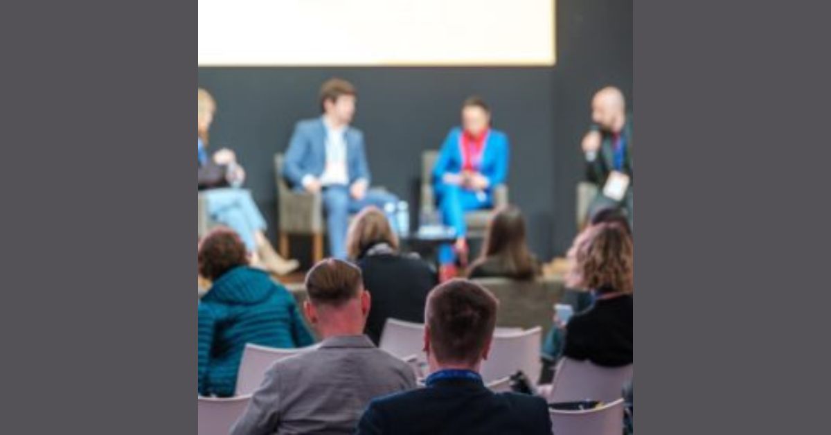 A diverse group of people seated in chairs, engaged in discussion at a conference setting.